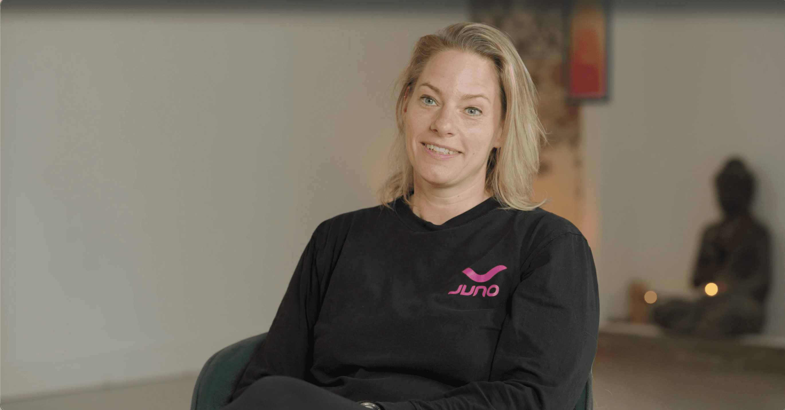 Synthia Stoffer zit in een stoel in haar sportruimte en kijkt lachend de camera in.